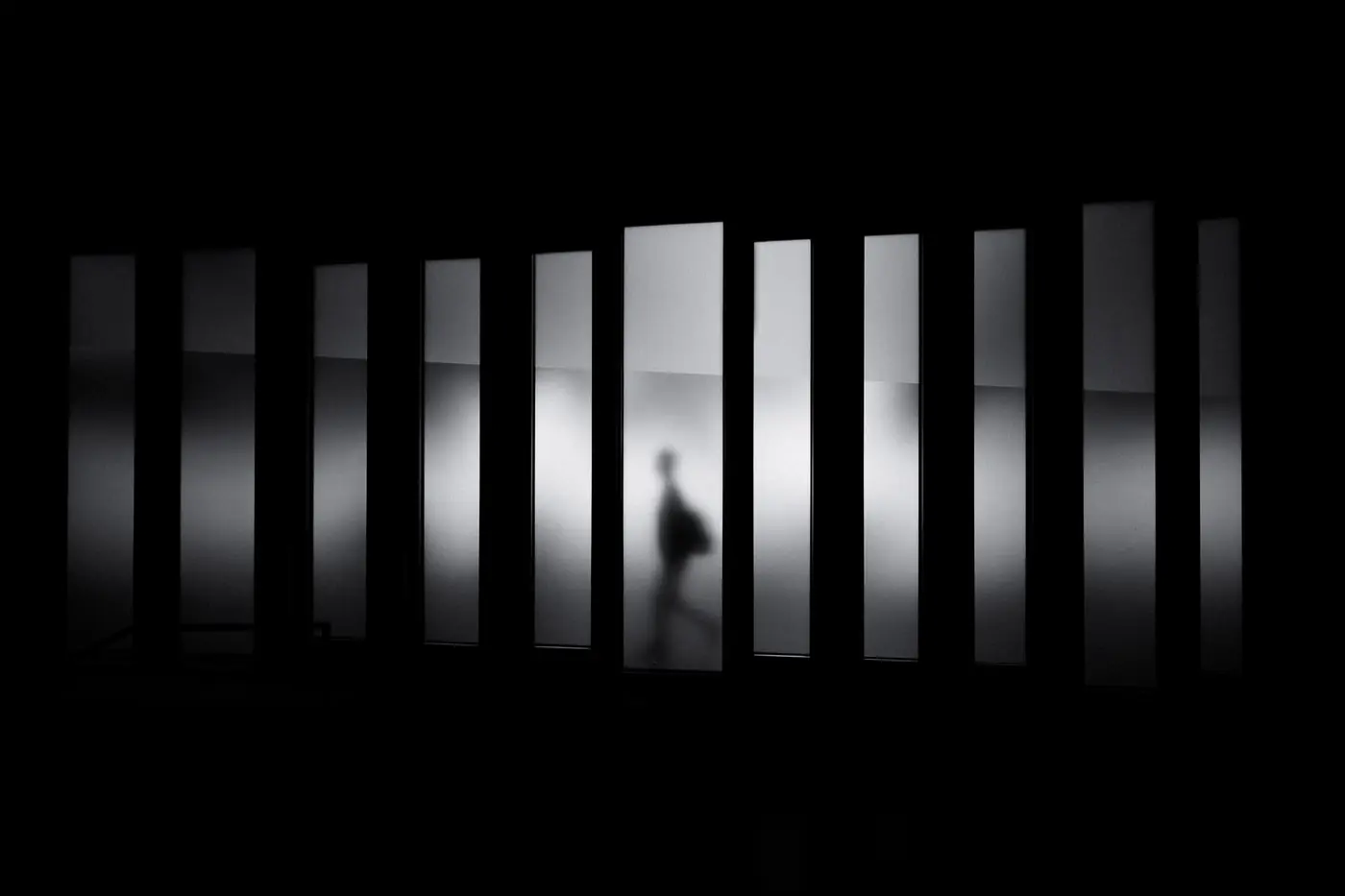 Silhouette of a person walking past tall illuminated windows